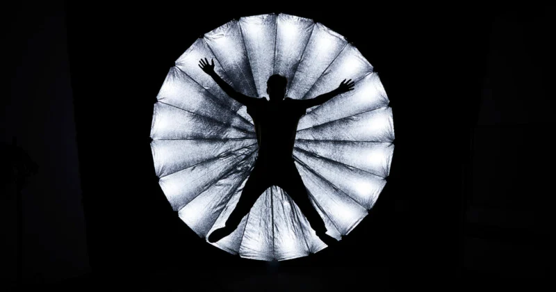 A person standing inside a large umbrella light, creating a dramatic silhouette effect against a dark background.
