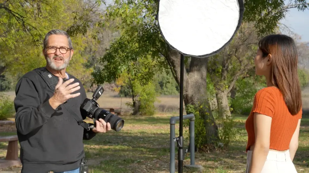 A photographer using a reflector to enhance natural light while shooting a model outdoors.