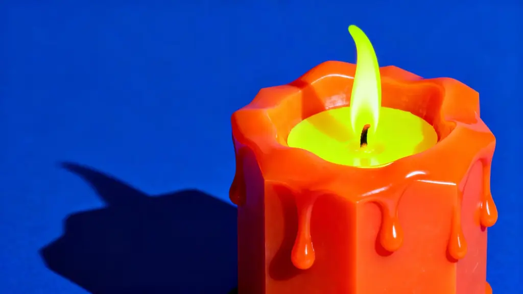 Close-up of a colorful candle with a bright orange wax and yellow flame, set against a vibrant blue background.