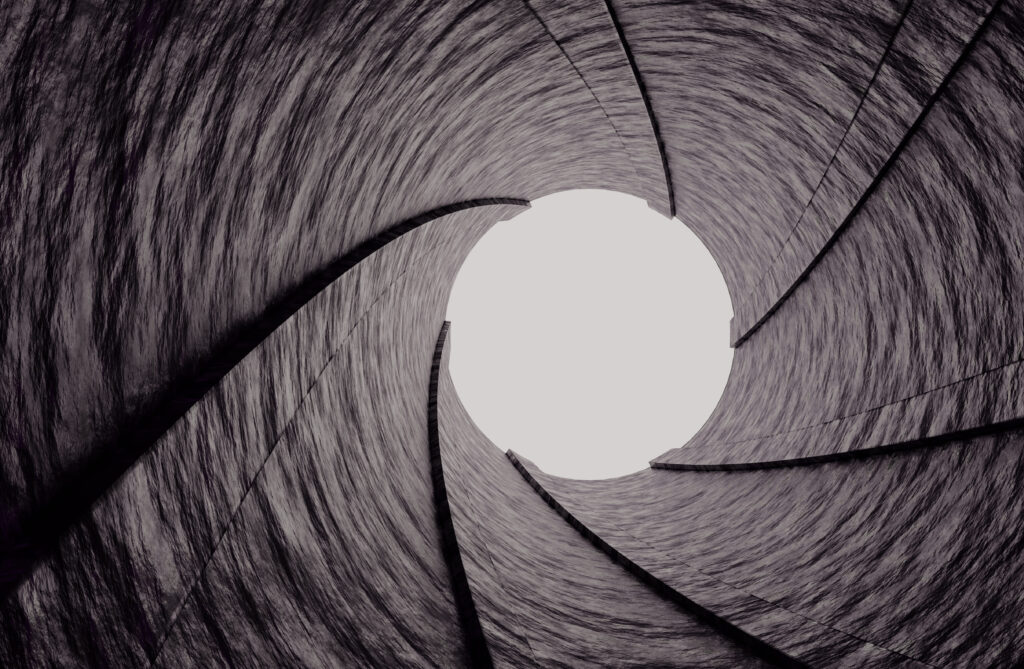  Close-up view of a camera shutter in a spiral motion, creating a tunnel-like effect leading to a bright center.