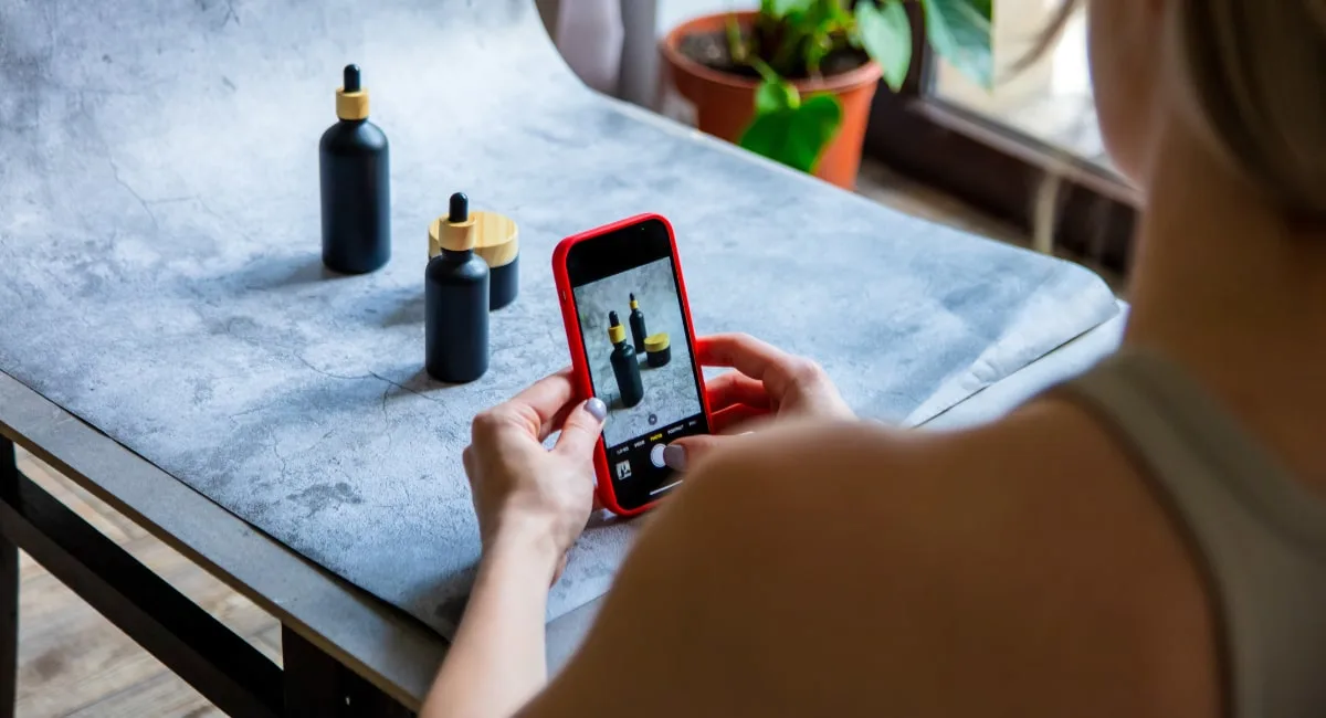 Person taking a photo of product bottles with a smartphone on a textured surface