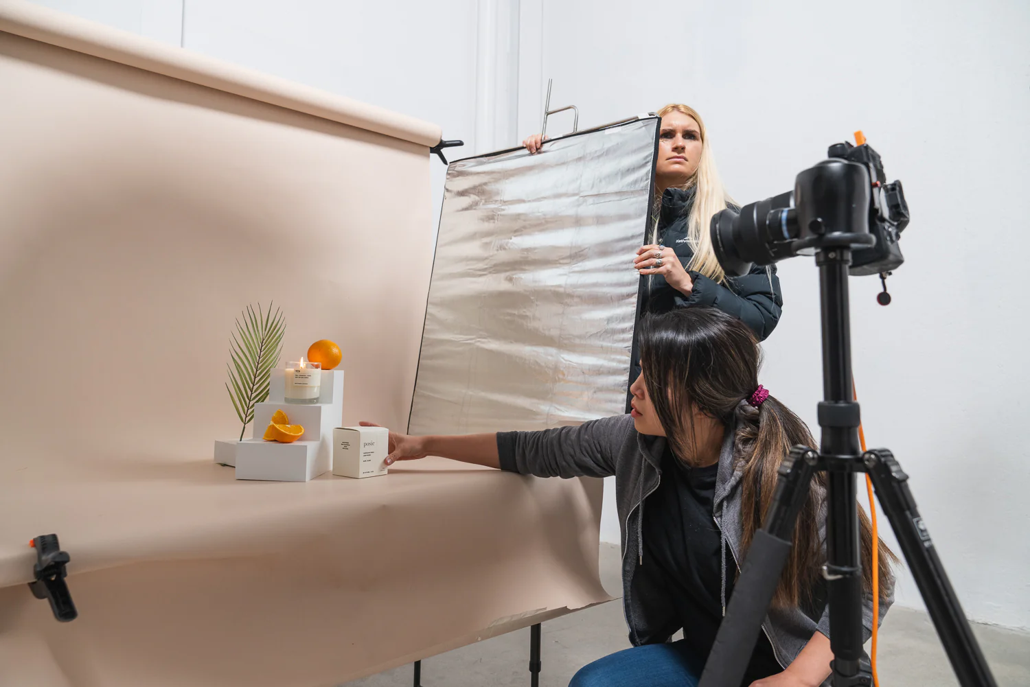 Two people working in a photography studio, arranging products and adjusting lighting for a product shoot.