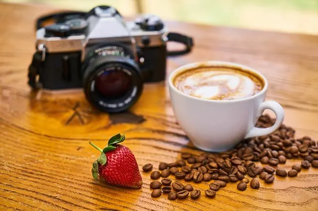 a cup of coffee, coffee beans, a strawberry and a camera on a wooden table which is the best camera for product photography