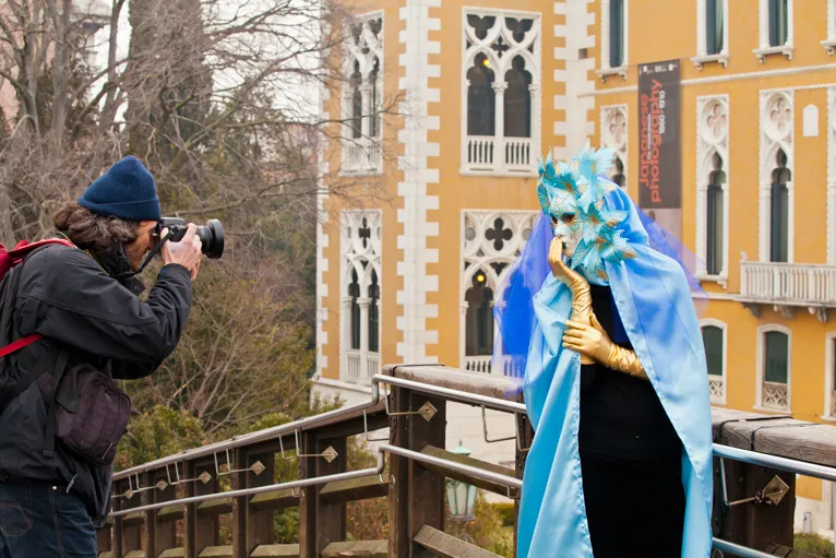 A photographer captures a person wearing a colorful mask and costume during an outdoor photoshoot.