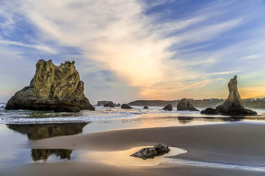  A scenic view of rugged rocks on a beach with a vibrant sky, reflecting in the calm water at sunset.