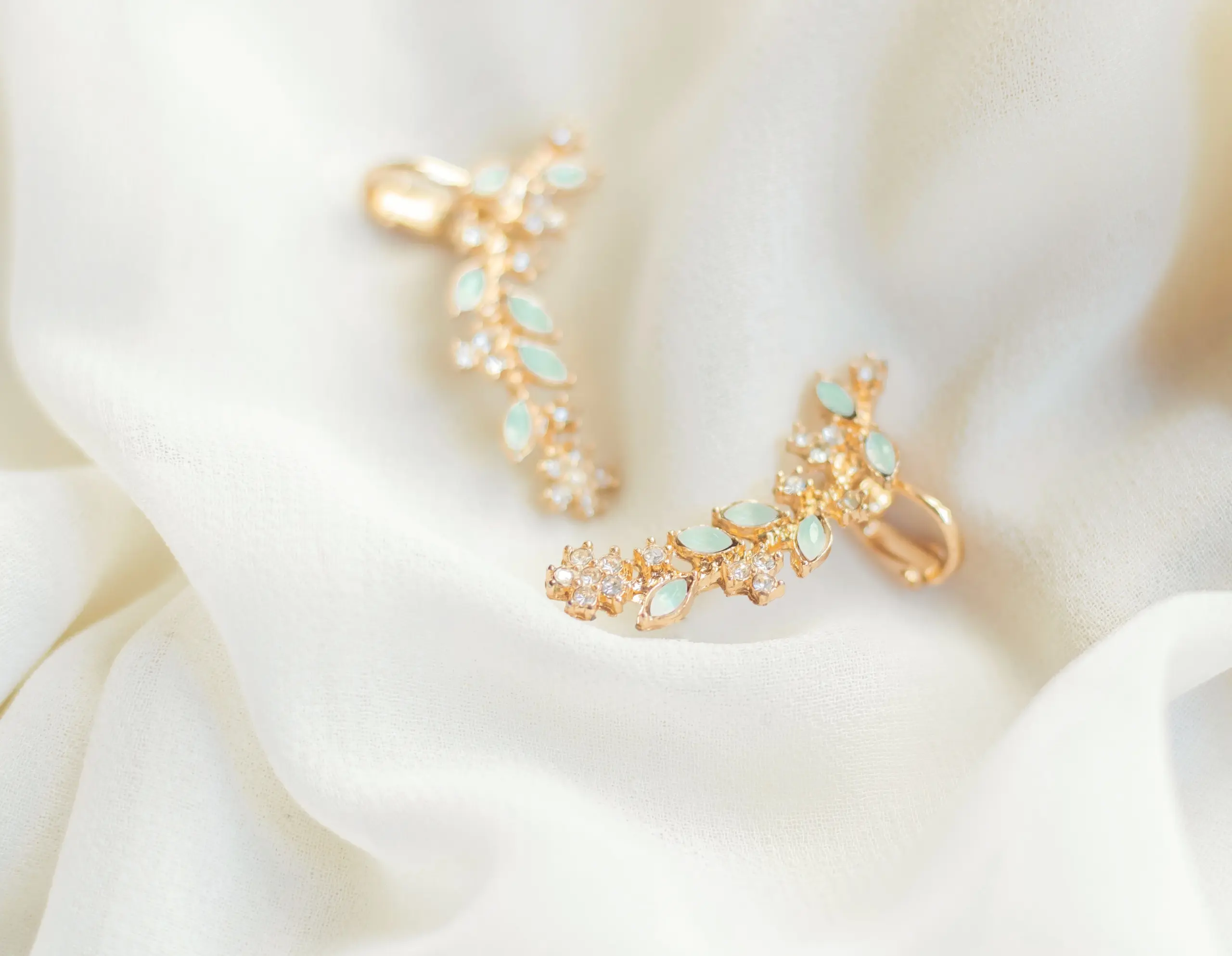 Close-up shot of gold earrings with green gemstones on a soft white fabric.