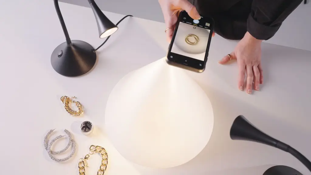 Person photographing jewelry with a smartphone under soft lighting setup.