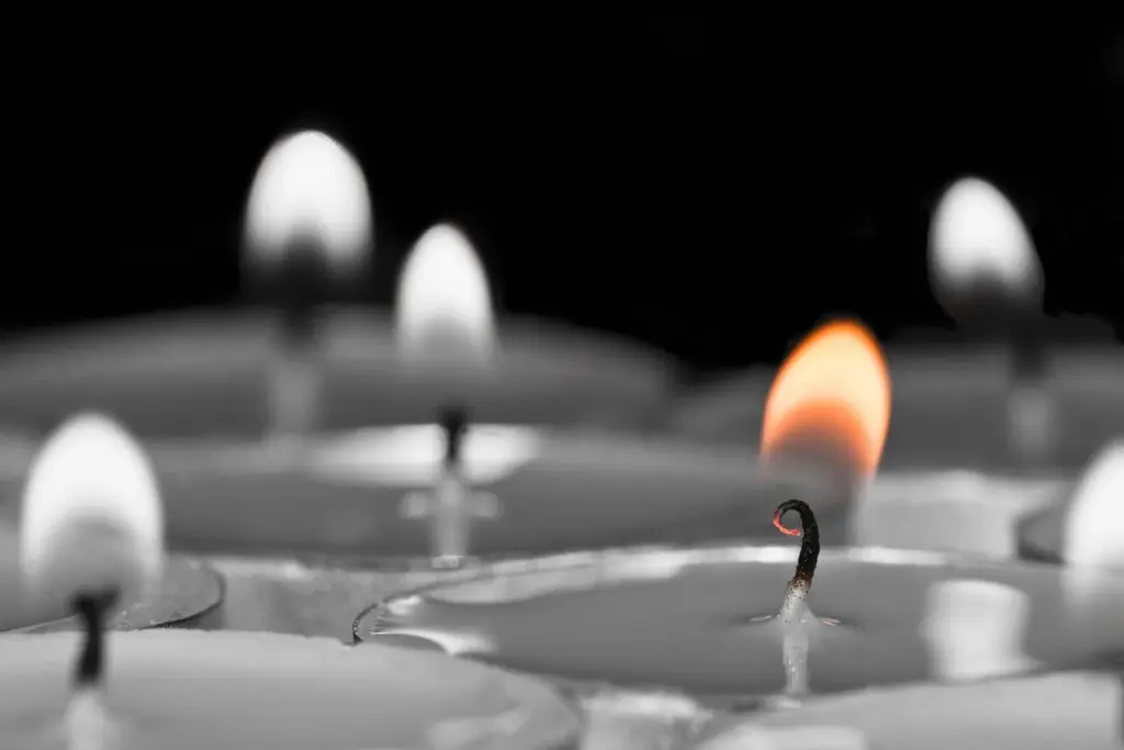 Close-up of lit and unlit candles with a blurred background, highlighting a single flame.
