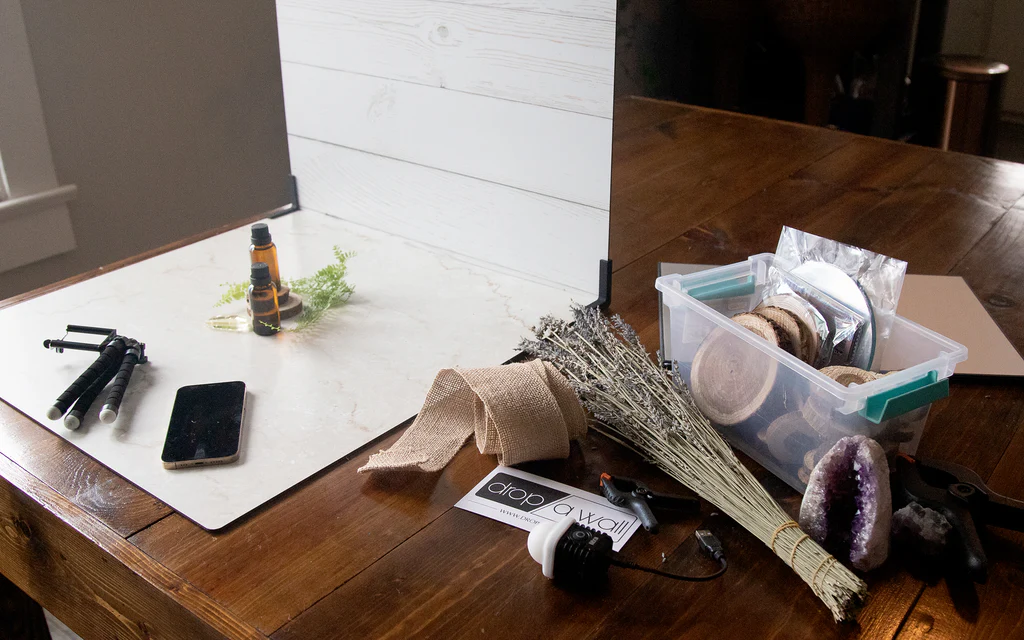 Photo setup with various props, including a phone, essential oils, wooden slices, and a backdrop, ready for still life photography.