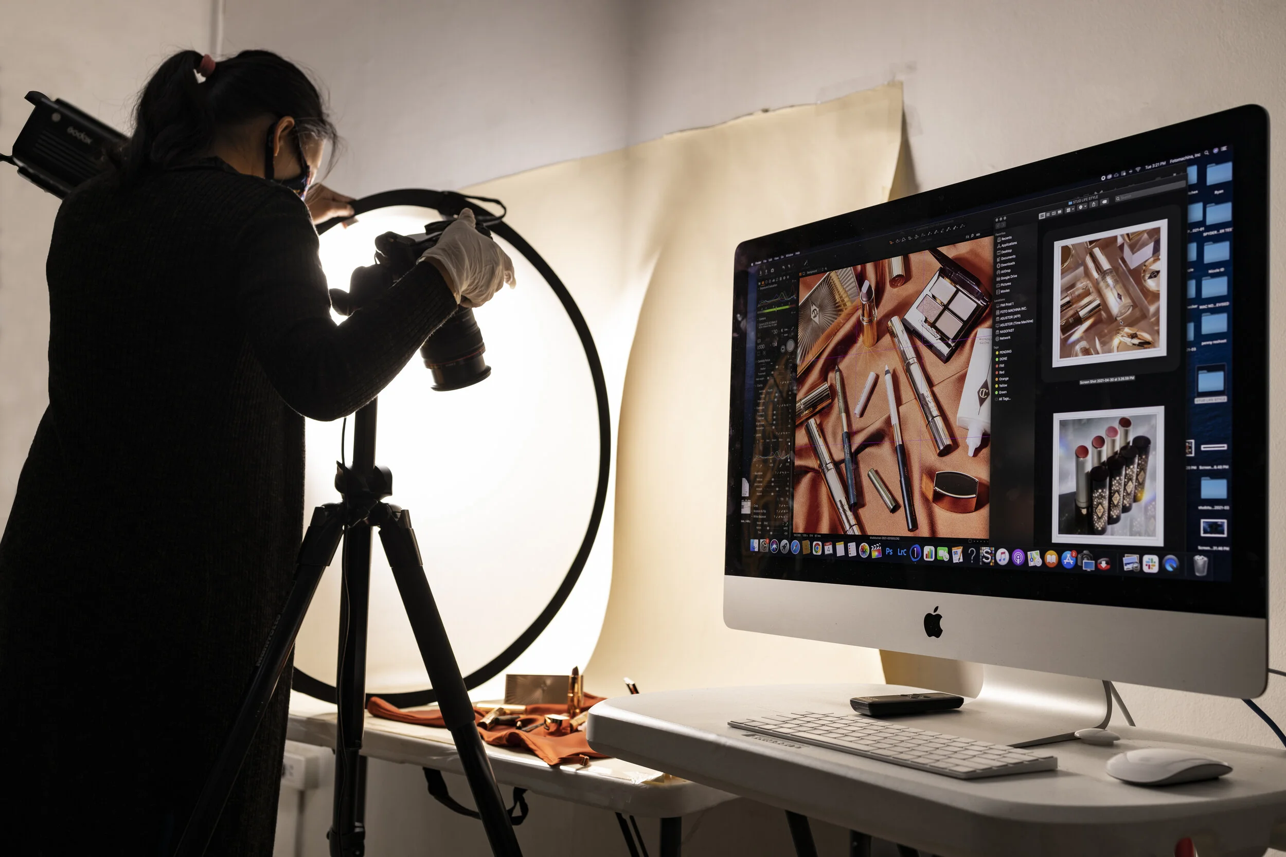 Photographer adjusting camera settings while capturing cosmetic products, with the live image displayed on an iMac.