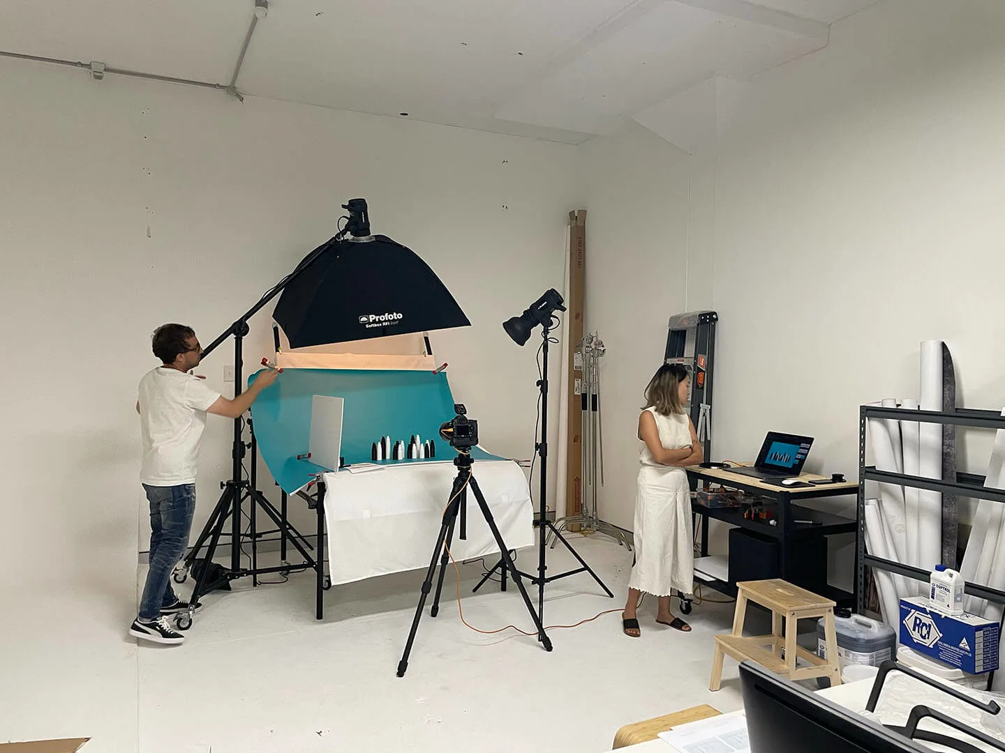a photography studio with two people working. One is adjusting a colorful backdrop, while the other monitors the shoot on a computer