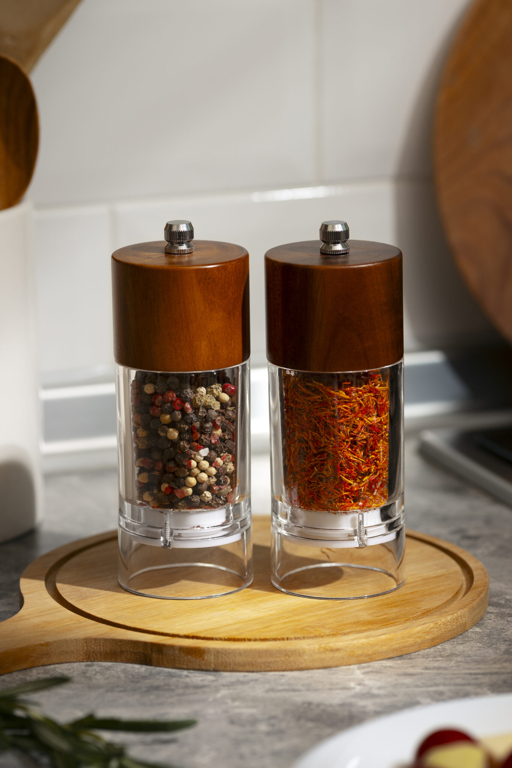 Close-up of pepper and spice grinders with colorful peppercorns on a wooden base.