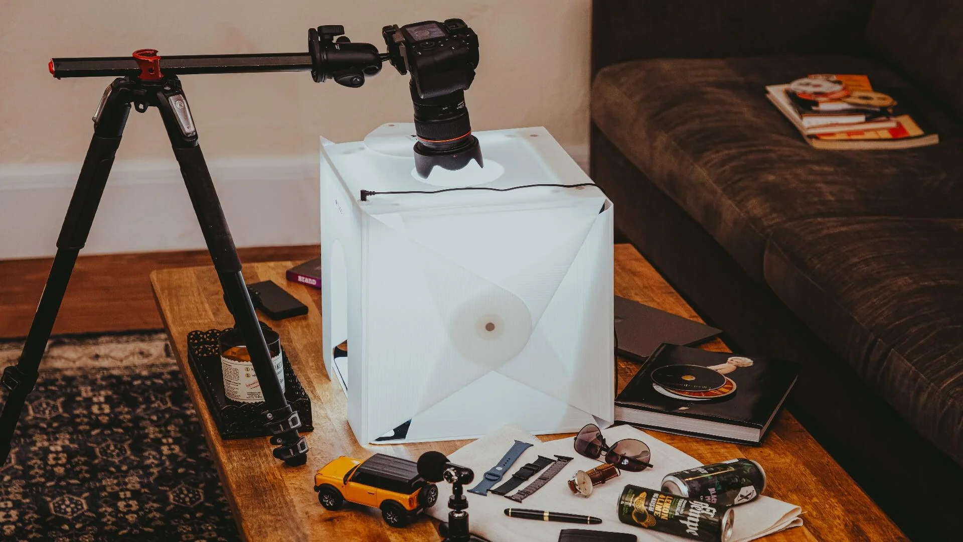 A flat lay product photography setup with a camera on a tripod capturing items inside a lightbox.
