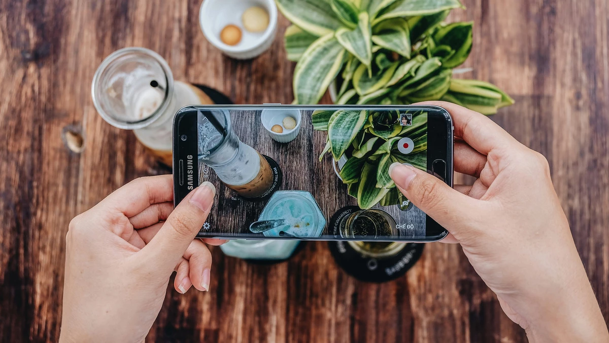 A person taking a photo of drinks and plants with a smartphone.