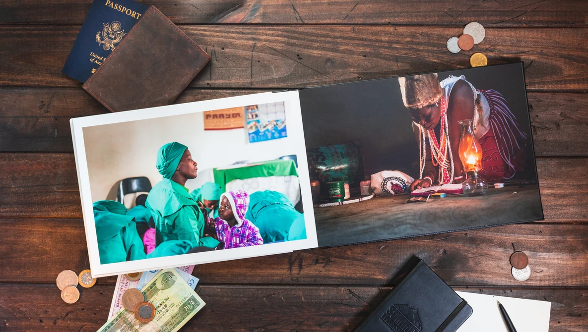 An overhead shot of a photo album with two pictures, set on a wooden table with a passport, coins, banknotes, and a notebook.