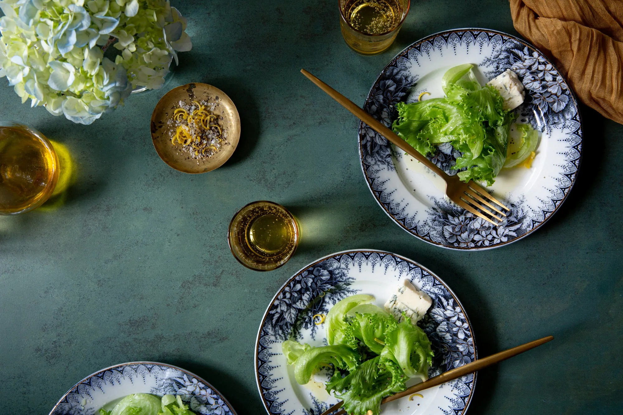 An overhead shot of salad plates, drinks, and a decorative dish, set on a vinyl surface with a textured green background.