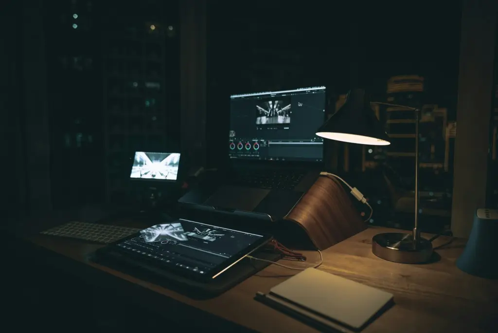  Dimly lit workspace at night with a laptop, tablet, and desk lamp, perfect for editing and post-production work.