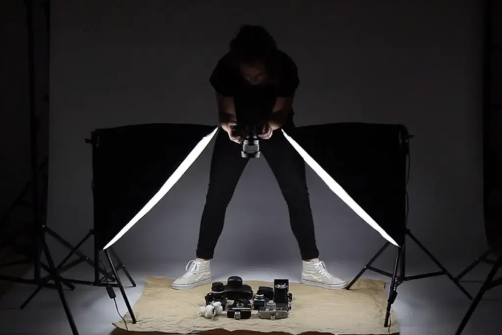 Female photographer crouching with camera between two softbox lights; lenses and gear on beige fabric