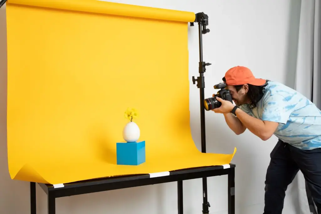 Types of product photography showing a photographer capturing an egg with a flower on a blue block against a bright yellow background.