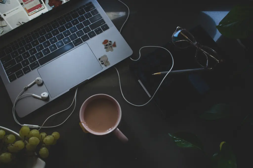 Photography workspace flat lay with MacBook, tea, AirPods, and panda stickers on dark surface. 