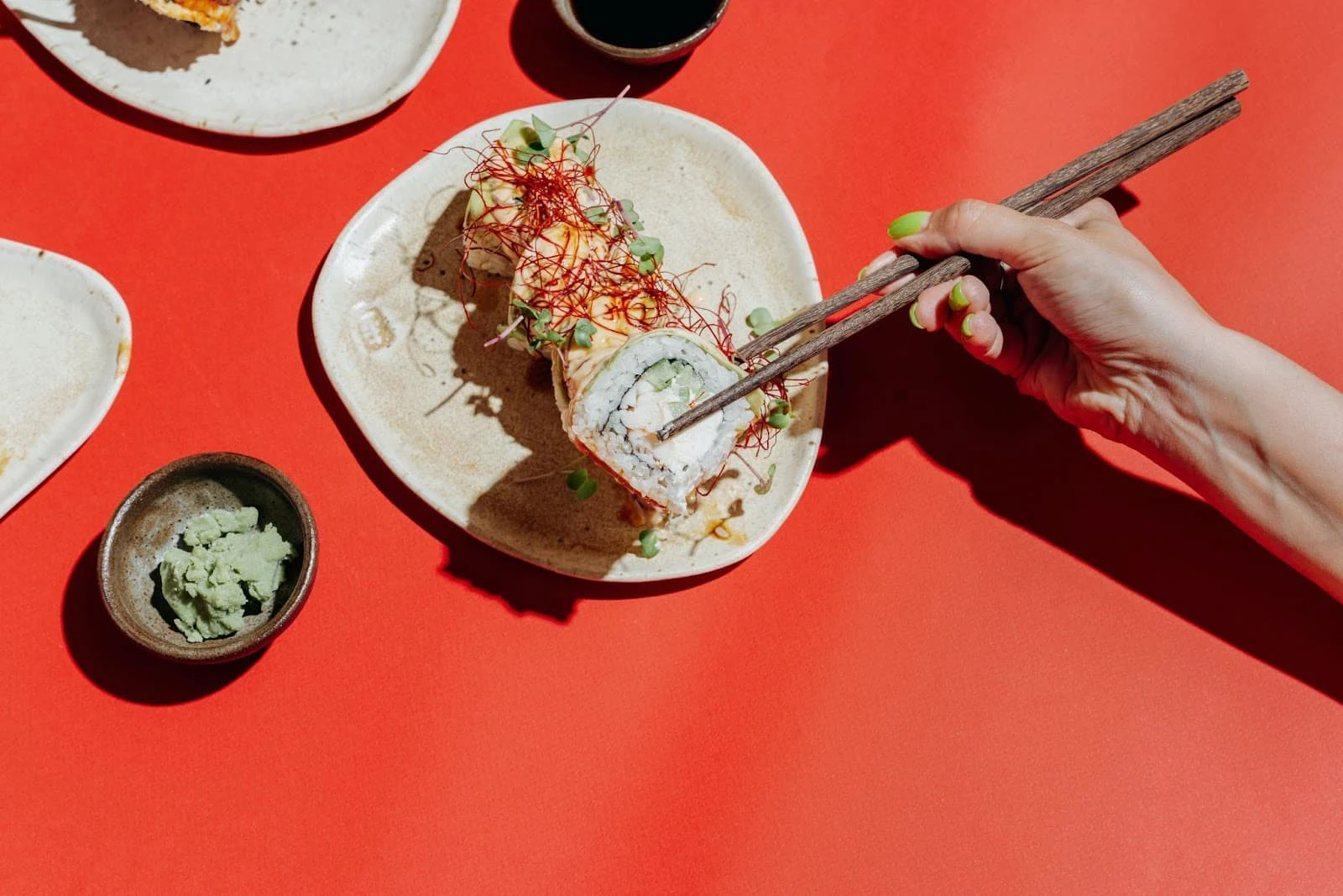 Hand holding chopsticks picking up a sushi roll on a plate with red background.