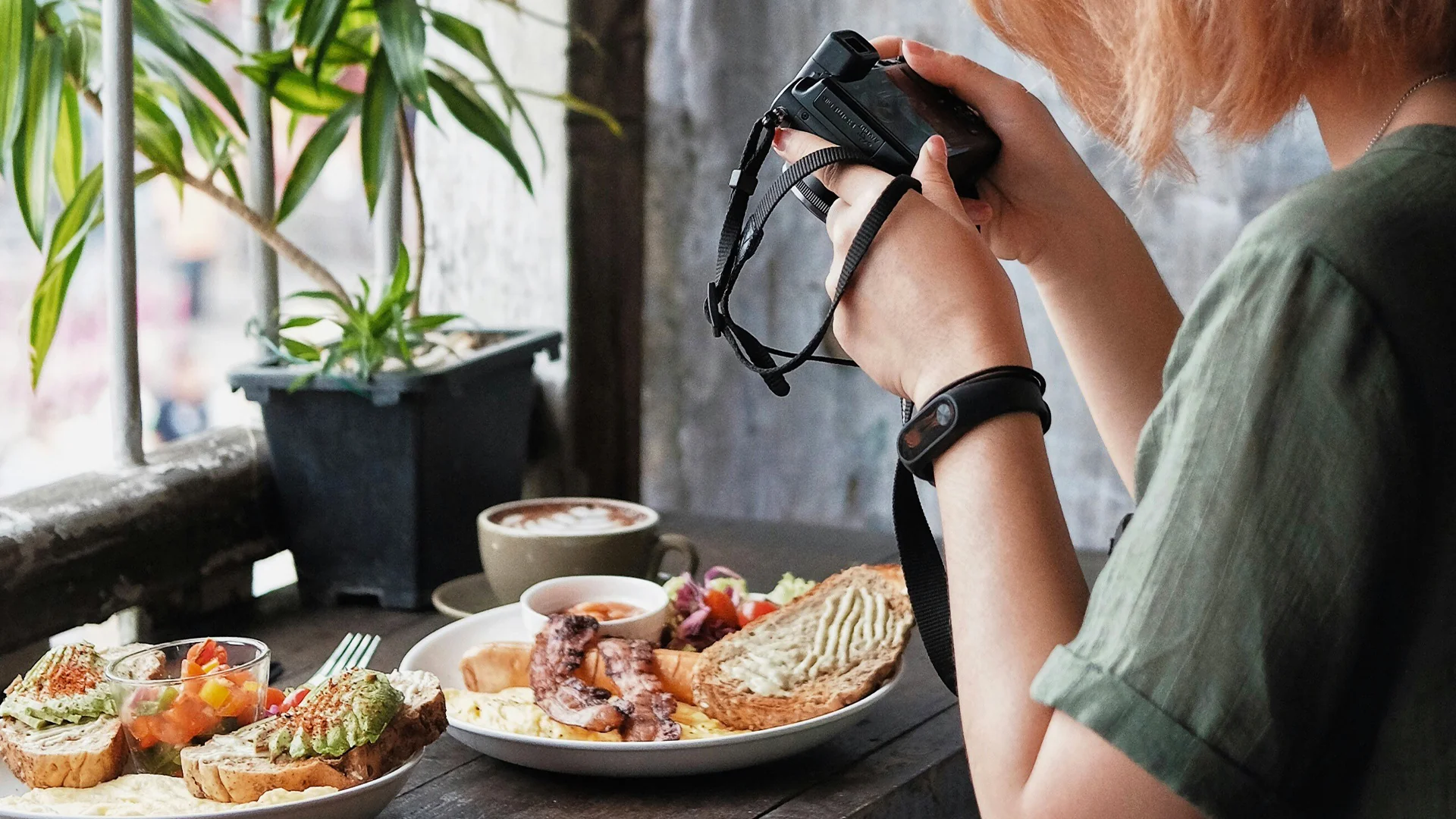 Person photographing a breakfast spread using a camera with natural lighting coming through a window