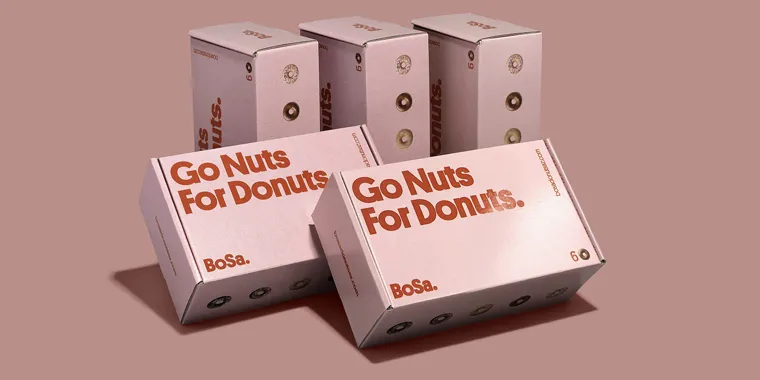 Pink donut boxes with “Go Nuts For Donuts” branding arranged on a muted pink background.