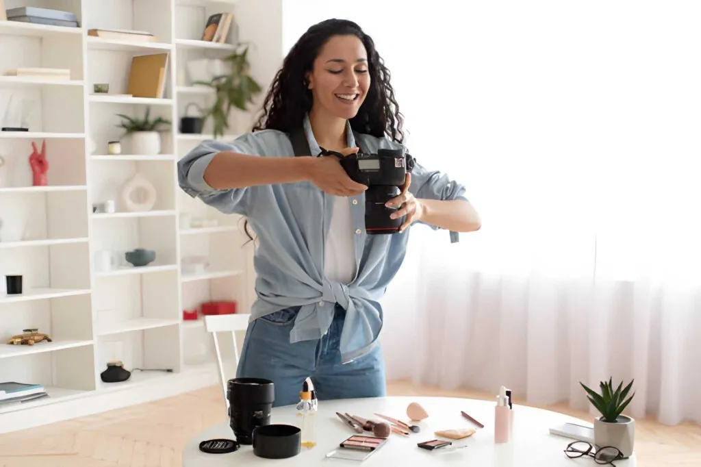 Smiling photographer holding a camera over a desk with makeup products arranged for a beauty product shoot.