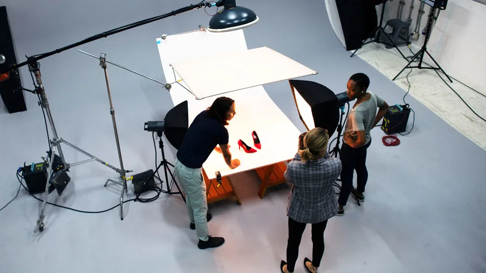 Product photography team using flash lights and softboxes to photograph red shoes in a studio setup.