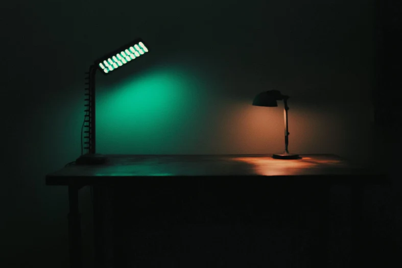 Two desk lamps casting green and warm orange light across a dark tabletop.