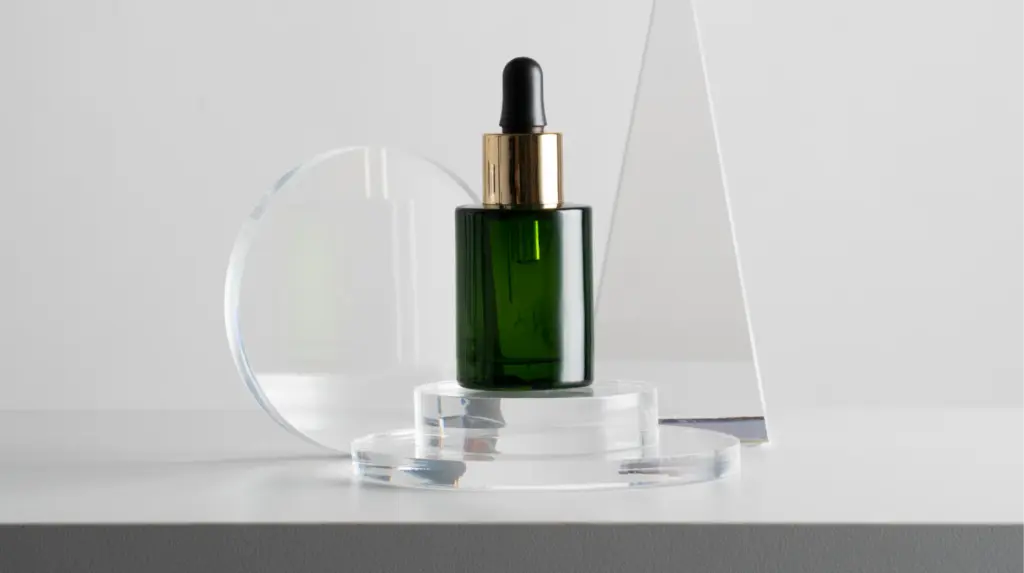 Green glass dropper bottle displayed on clear acrylic stands for transparent product photography.