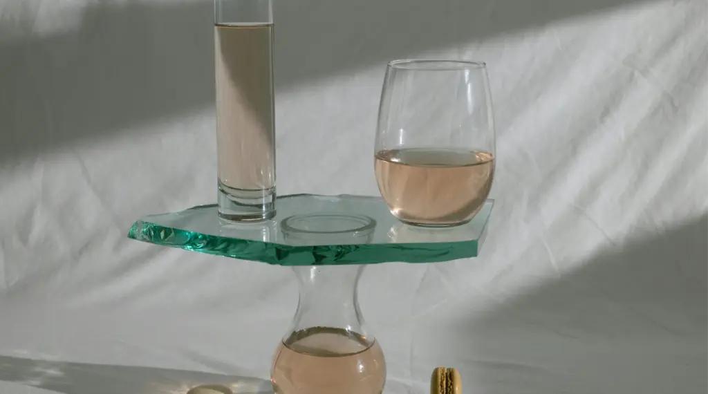 Transparent glassware with soft pink liquid arranged on a reflective glass surface for product photography.